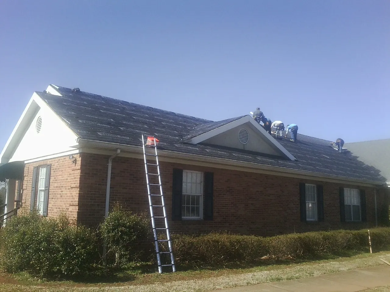 Crew tearing shingles off a brick ranch roof with a ladder set — Emergency Roof Repair work by our crew in Callicoon Center