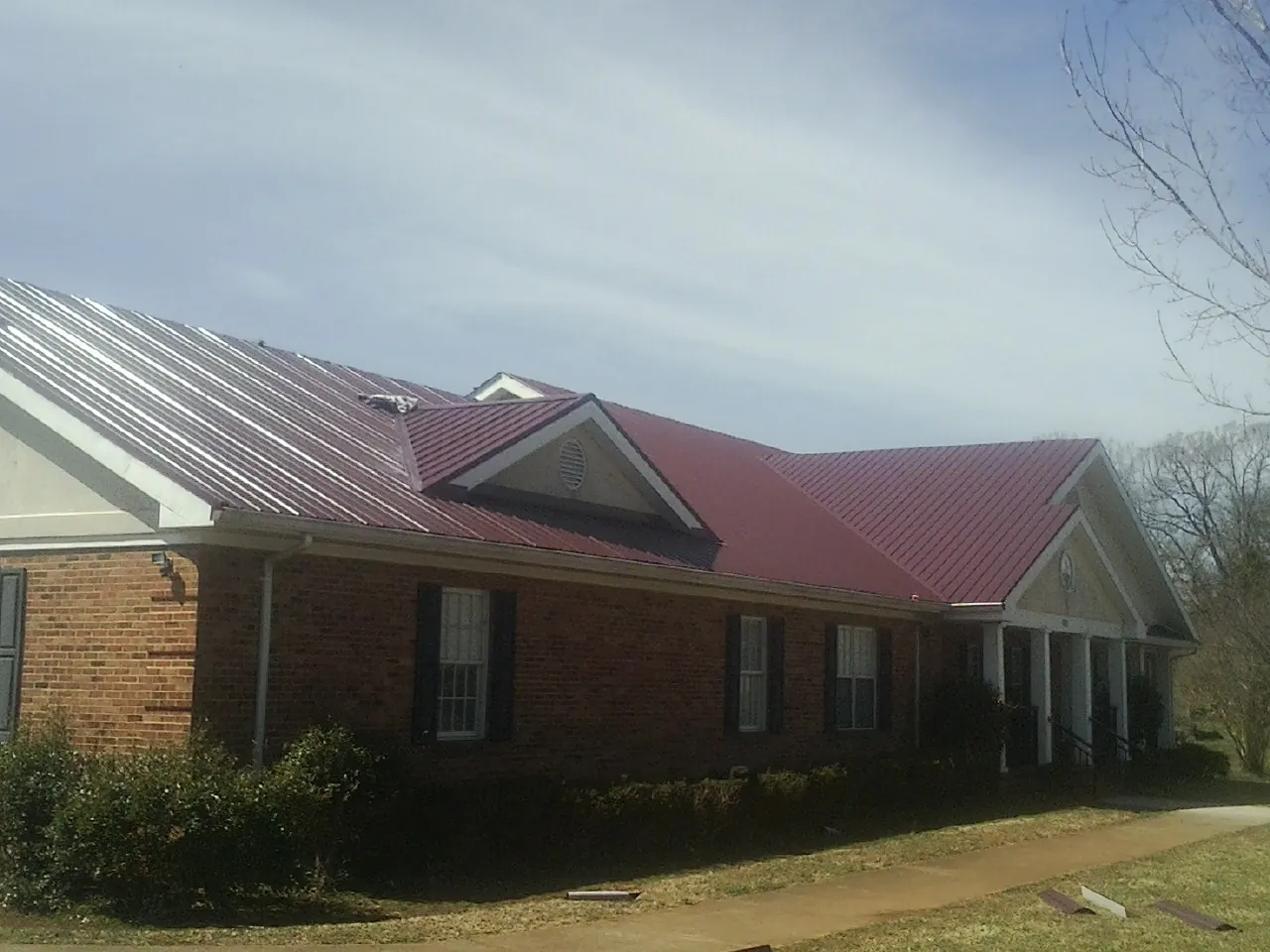 Red metal roof with gabled entries on a long brick building, from a Hail Damage Roof Repair job in Callicoon Center