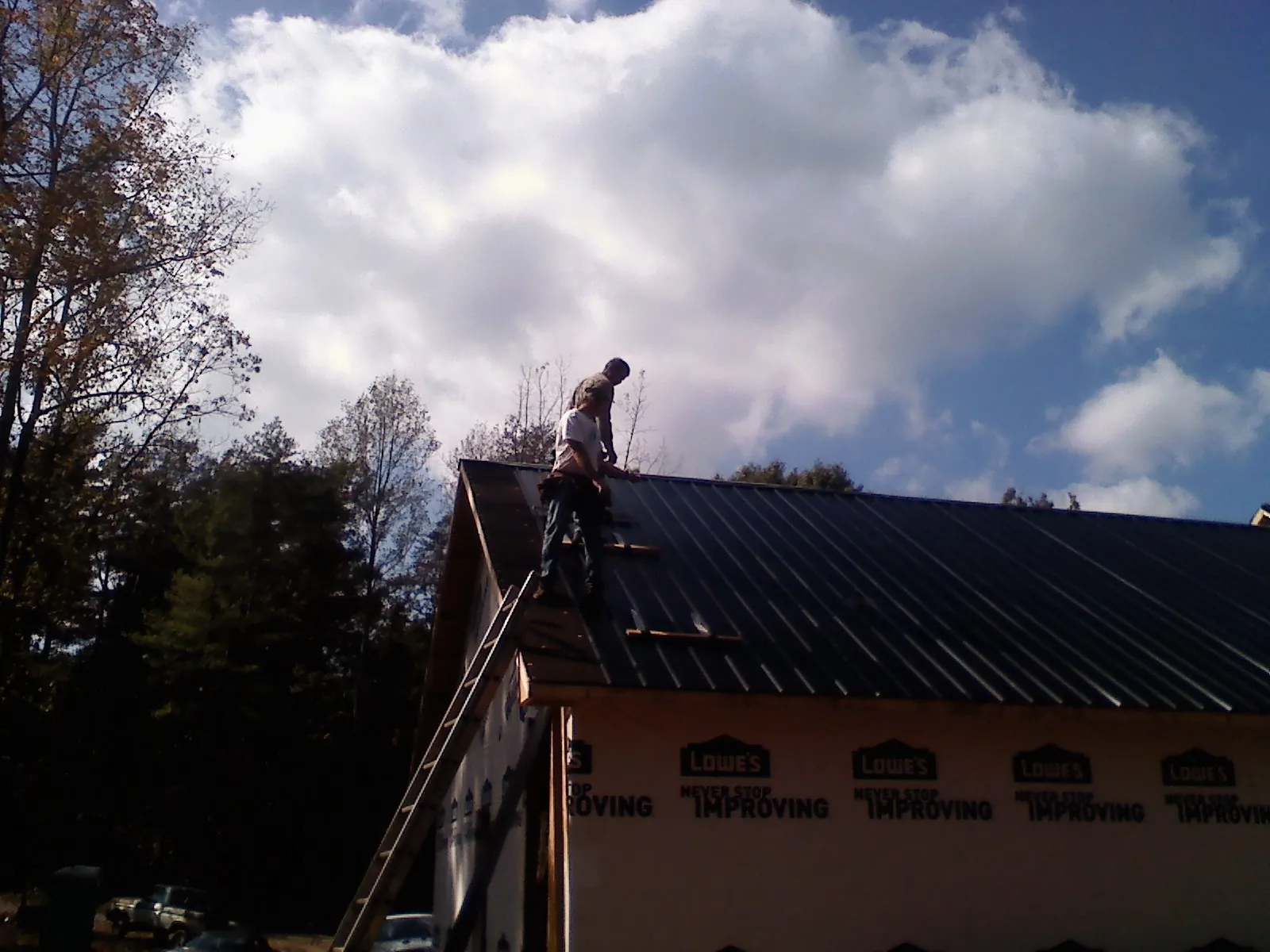 Roofer fastening dark metal panels high against a cloudy sky, from a Roof Inspection job in Callicoon Center