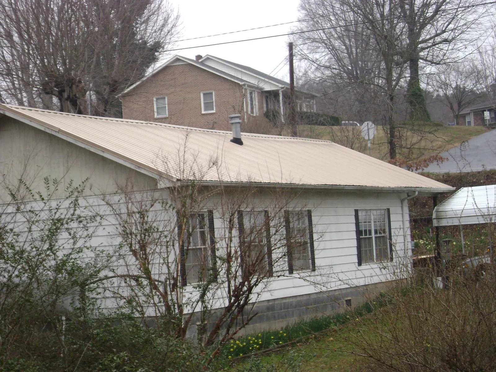 Tan metal roof on a white sided house set into a hillside — Commercial Roofing by Roofing Brothers in Callicoon Center